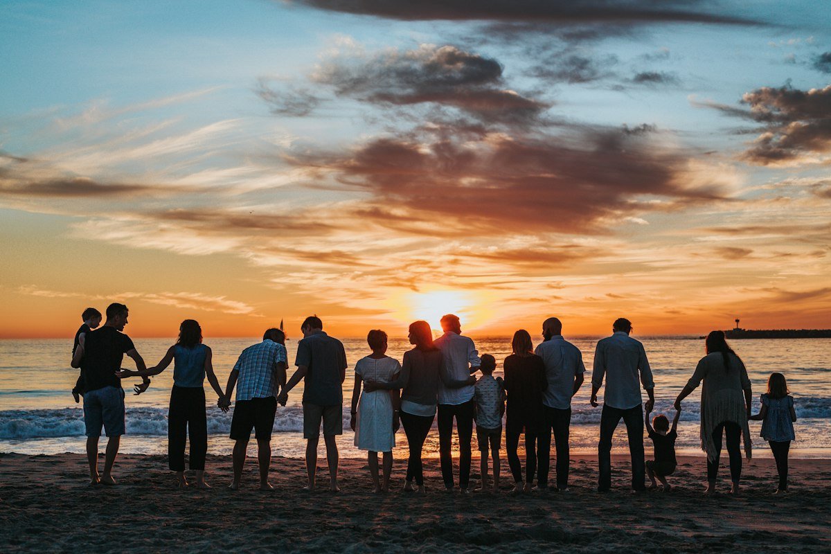 Three generations of a family holding hands on a beach at sunset